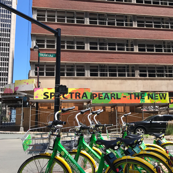 Green and yellow Hartford City Bikes with Colorful Sign in the Background on Brick Historic Building